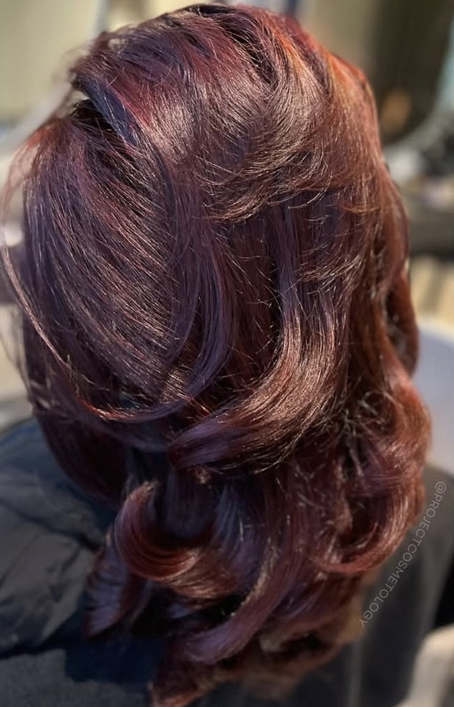 Shiny, curled burgundy hair with highlights.