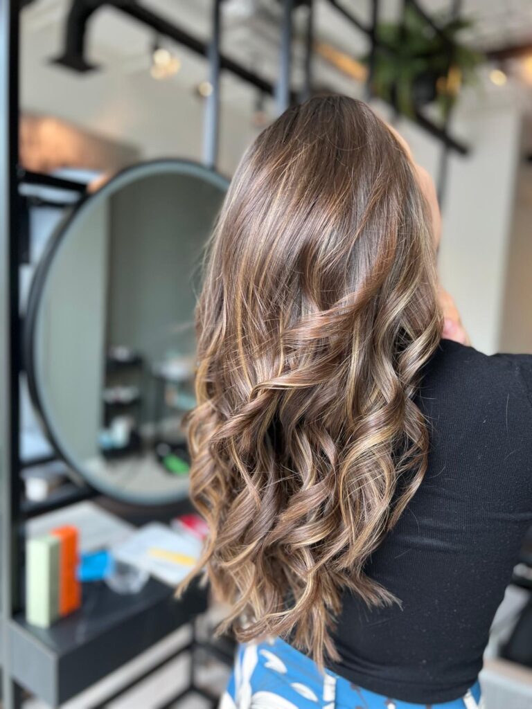 Woman with curly hairstyle in salon mirror reflection.